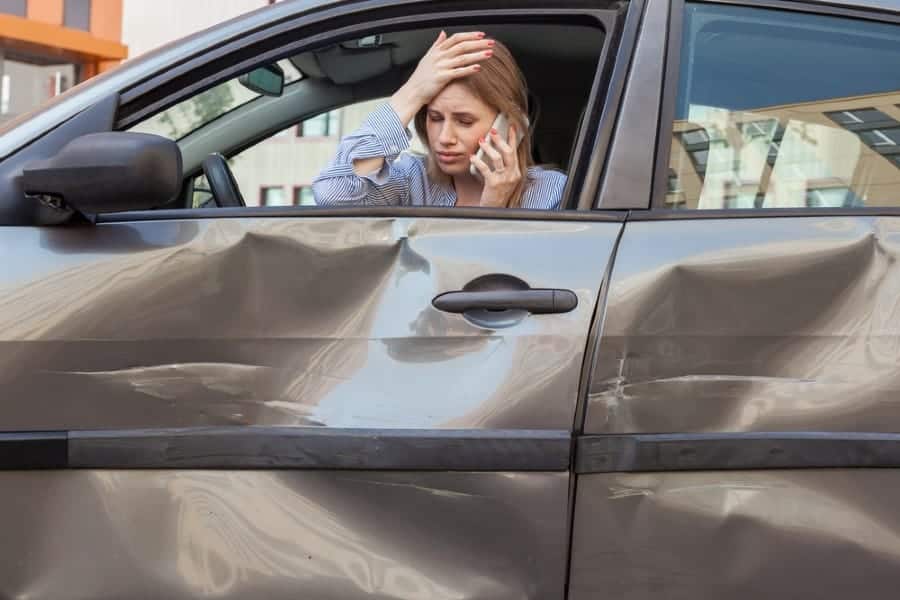 woman in car accident holding her head while on a cell phone